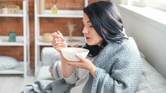Sick mature woman eating chicken soup at home